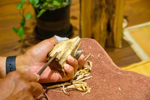 Hands hold and inspect a piece of agarwood wood on a brown cloth during a fragrance workshop in Hanoi