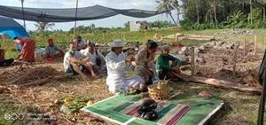 Priest and guests seated on woven rugs with ceremonial offerings outdoors at Omunity Bali in Bali during a cleansing ceremony