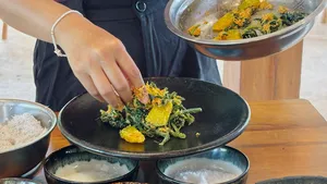 Chef-led vegan cooking prep, adding chopped greens and spices to a black frying pan on a wooden table in Labuan Bajo
