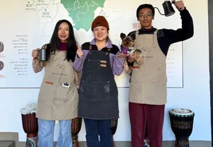 Guests in aprons posing with a small dog in front of a Yunnan coffee map at a coffee workshop in Lijiang