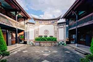 Pintu gerbang laman tradisional Bai di Linden Centre, Pekan Lama Xizhou, Dali, membingkai patio batu dan perincian ukiran biru-putih
