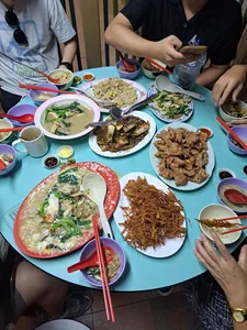 Shared table of Cantonese hawker dishes in Singapore, diners using chopsticks and bowls as food is served family-style