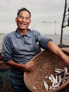 Ha smiling beside a woven basket of small fish at the coast in Hoi An, sharing local morning fishing traditions