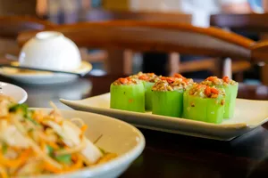 Stuffed green gourd pieces topped with herbs on a serving tray, with other dishes at an indoor Hanoi tasting meal