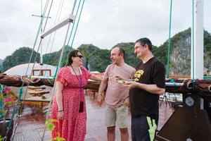 Travellers chatting on the deck of a boutique wooden cruise in Cat Ba National Park, with limestone cliffs across the bay