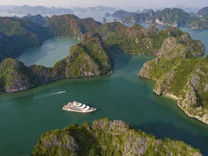 Aerial view of limestone karst islands and a cruise ship gliding through turquoise waters in Halong Bay