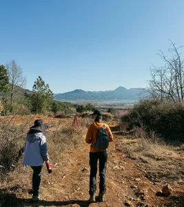 Backpackers trekking along a rural path outside Lijiang, with hazy mountains and a broad valley stretching in the distance
