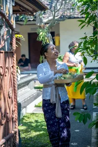 Balinese woman arranging canang sari offerings with flowers and incense in a garden courtyard, during a Ubud ceremony