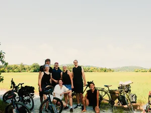 Bicycle Day Langkawi group photo in a sunlit field on Langkawi, posing with bicycles and camping gear by the roadside