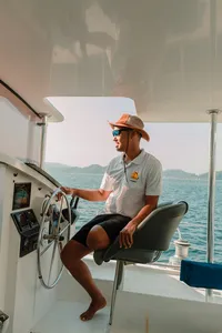 Jerry Reichart of Mawali Sailing steering a catamaran on the sea off Kota Kinabalu, with distant hills in view