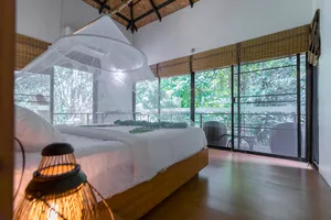 Sheer-canopy bed inside Anurak Lodge at Khao Sok National Park, with open windows framing the surrounding rainforest