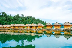 Rows of riverside thatched cottages reflected on Cheow Lan Lake at Khao Sok Riverside Cottages, a family-run stay