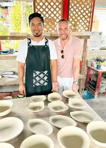 Two pottery makers at Ilham Ceramic Studio in Langkawi arrange white ceramic bowls on a workbench during a workshop