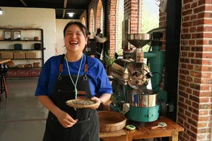 Host-led specialty coffee workshop at Seeker Yunnan Coffee Estate, Lijiang: woman holds a tray of roasted beans beside a roaster