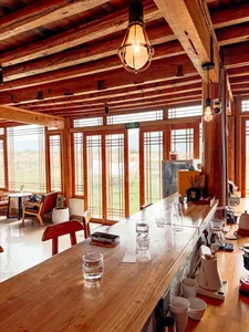 Sunlit interior of a family-run coffee workshop in Lijiang, with a long wooden tasting table, hanging lamps and countryside views