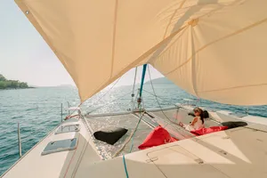 Catamaran sail across the water off Kota Kinabalu, a passenger resting under the cream sail canopy — Mawali Sailing