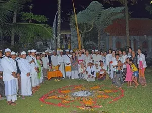 Participants in white ceremonial clothing gather around a flower mandala for a sacred ritual in the garden at Omunity Bali, Bali