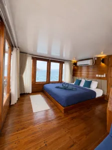Blue-dressed beds in a wooden cabin with sea-facing windows on board the 3D2N shared Komodo cruise, Komodo Island