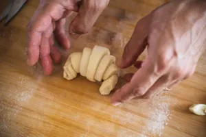 Hands portioning and rolling croissant dough on a floured wooden worktop in a home kitchen in Singapore — workshops in Singapore