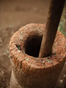 Close-up of a wooden pestle turning in a large clay mortar, with small herb pieces on the rim in Lombok village food prep