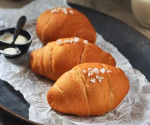 Golden shio pan buns on parchment-lined tray with a small cup of pale butter nearby, ready to bake in Singapore