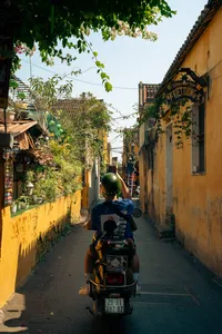 Perjalanan Vespa berpemandu melewati gang sempit yang dipenuhi tanaman di Hoi An, dengan papan suvenir di sepanjang jalan kota tua