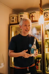 SakeMama smiling and holding a bottle for rare sake tasting in a tucked-away Singapore shop with other brews — Singapore hidden gems