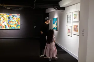 Two visitors walking past framed artworks in a narrow corridor at Quang San Art Museum on a Vietnamese art tour in Ho Chi Minh City