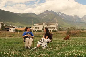 Outdoor coffee tasting with Seeker Yunnan Coffee Estate host and guest in Lijiang, surrounded by wildflowers and mountains