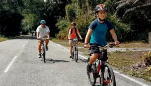 Cyclists ride a rural road through dense greenery, with a rider in the foreground during a jungle cycling trip near Kuching