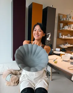 Ina Atelier potter smiling while holding a European-style ceramic plate with scalloped texture in the Singapore studio