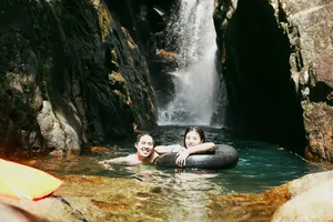 Couple laughing as they float in an inner tube at a hidden Hoi An waterfall, surrounded by wet rock walls