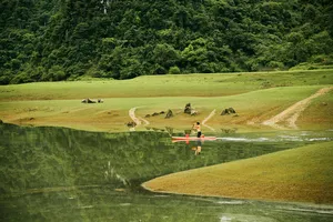 Aerial view of a small orange boat crossing a calm green lake through open valley scenery on the Cao Bang motorbike loop