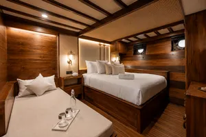 Travass Life new phinisi cabin interior with two twin beds, wooden wall panels, lamps and porthole windows for a Komodo Island trip