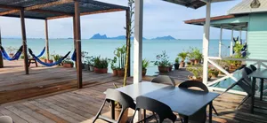 Meja makan dan buaian gantung di dek kayu banglo air di Semporna, dengan laut terbuka dan pulau-pulau di kejauhan