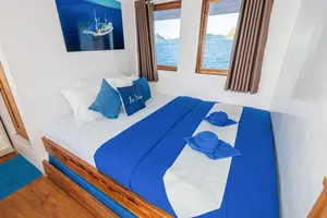 La Famille cabin with blue-and-white bedding and sea-view windows aboard a Komodo boat trip, Labuan Bajo
