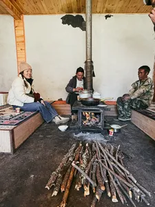People warming by a wood-fired stove with pots in a guesthouse kitchen in Lijiang during the Yi & Naxi village trek