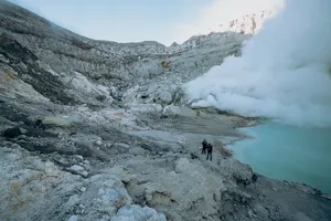 Hikers on the rocky rim of Mt Ijen at sunrise, watching the blue crater lake vents, on a 3D2N trip from Banyuwangi