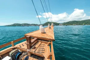 Private 3D2N Komodo cruise on a sleek white phinisi: wooden stern bench and ropes overlooking the coastline in Labuan Bajo