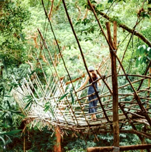 Ngapuh Homestead builder in a hat working among bamboo and branches in the forest, rainforest tones near Kuching