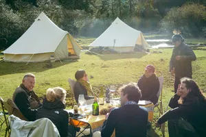 Travellers sharing dinner at a valley camp with white tents and glowing lanterns, part of a caravan trek stay near Shangri-La