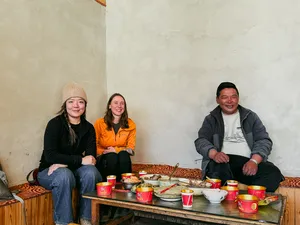 Three guests seated indoors around a shared meal with red cups at a Lijiang guesthouse during a Yi & Naxi village trek