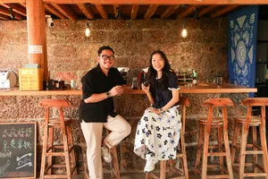 Hosts smiling behind the bar with coffee equipment in a stone-walled Lijiang coffee workshop for Seeker Yunnan Coffee Estate