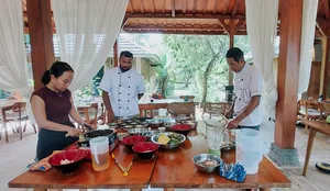 Small group cooking around pans and bowls, learning vegan Manggarai dishes from a local chef during a class in Labuan Bajo