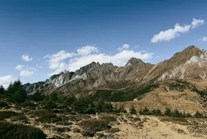 Jade Dragon Snow Mountain ridgeline near Lijiang under a blue sky, with rocky slopes and scattered evergreen trees