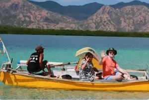 People seated on a yellow boat over clear turquoise water with hills in the distance, on a Komodo day trip from Labuan Bajo