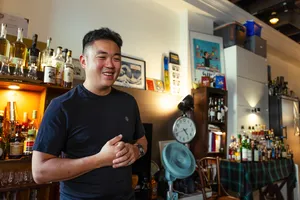 Scotch & Sambal host in a Singapore home bar smiles with a whisky glass, leading a small-batch tasting with bottles behind