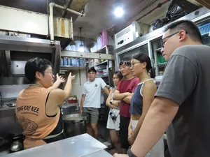 Pasar Fish host-led group inside a Singapore seafood stall kitchen, the guide gesturing as they learn about Cantonese fish