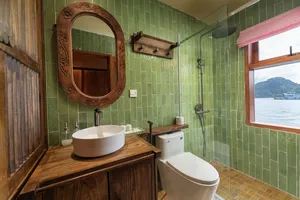 Green-tiled ensuite bathroom with a vanity sink, toilet and shower, plus a window view of the bay on Cat Ba Ocean Cruises