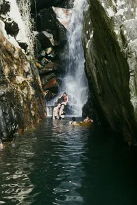 Swimmers in a misty hidden waterfall gorge, surrounded by steep cliffs on a secret waterfall trip from Hoi An